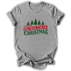 A heather gray short-sleeve t-shirt with a 'Nutcracker Christmas' graphic on the chest, featuring green pine trees and red and green text, displayed on a white background.