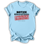 A light blue short-sleeve t-shirt with a graphic print that reads 'NOTICE Rehearsal Season: ATTENDANCE MANDATORY' in black and red text, displayed on a clean white background.