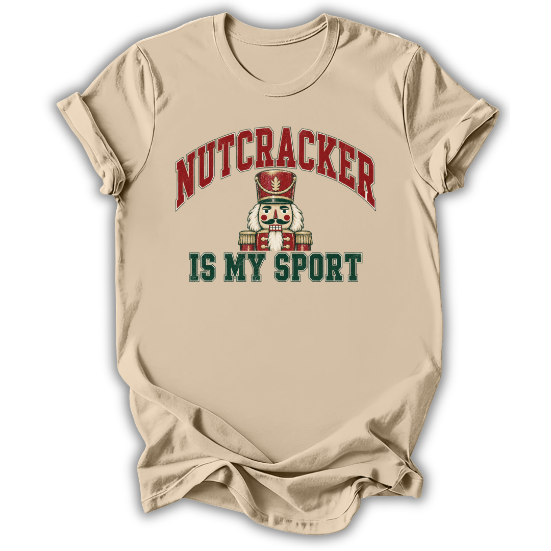 A beige short-sleeve t-shirt with a graphic print on the front. The graphic features the word 'NUTCRACKER' in red arched letters above a nutcracker illustration, and the phrase 'IS MY SPORT' in dark green block letters below.