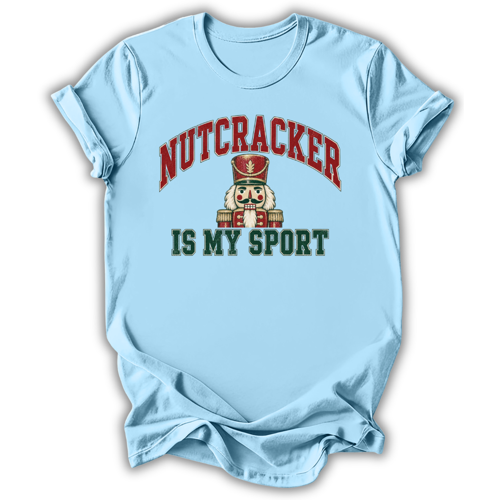 A light blue short-sleeve t-shirt with a graphic on the front that reads 'NUTCRACKER IS MY SPORT' in red and dark green lettering, featuring a nutcracker illustration in the center, shown on a white background.
