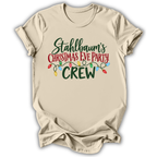 A beige short-sleeve t-shirt with a graphic print that reads 'Stahlbaum's Christmas Eve Party CREW' in green and red lettering, decorated with a string of multicolored Christmas lights, shown on a white background.