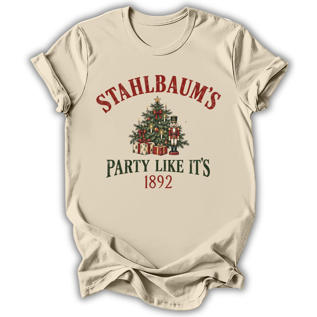 A beige short-sleeve t-shirt with a vintage Christmas graphic on the front. The graphic features the text 'STAHLBAUM'S PARTY LIKE IT'S 1892' in red and dark green lettering, surrounding an illustration of a decorated Christmas tree with gifts and nutcrackers.