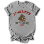 A heather gray short-sleeve t-shirt with a vintage-style Christmas graphic on the front. The graphic features the text 'STAHLBAUM'S PARTY LIKE IT'S 1892' in red and dark green lettering, surrounding an illustration of a decorated Christmas tree, gifts, and nutcrackers.