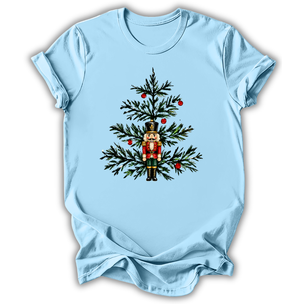 A light blue short-sleeve crewneck t-shirt with a graphic of a nutcracker standing in front of a decorated Christmas tree, shown on a plain white background.