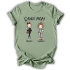 A sage green short-sleeve t-shirt with a graphic print that reads 'DANCE MOM' above two cartoon women labeled 'FRIDAY' and 'SUNDAY'. The shirt is shown flat against a white background with a soft drop shadow.