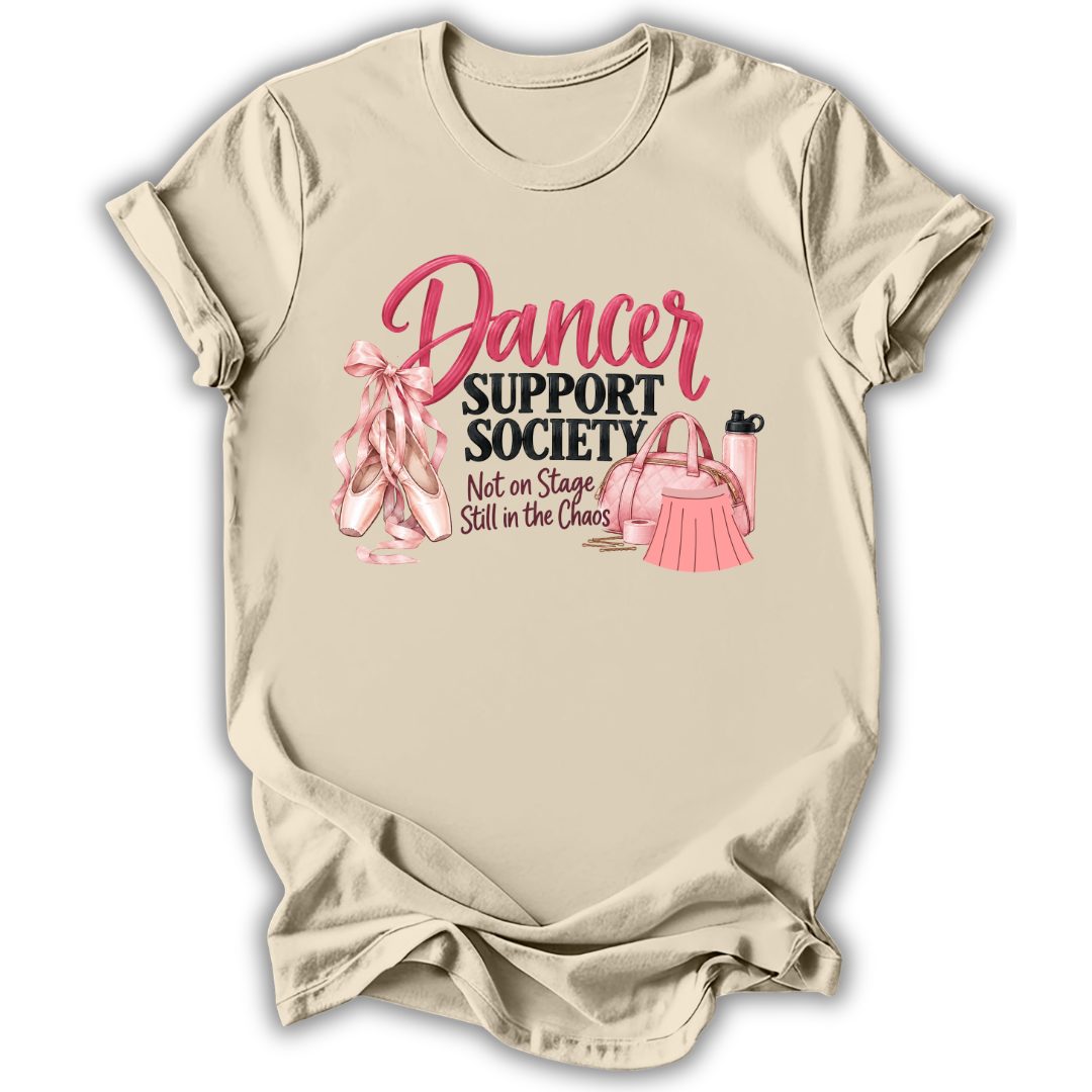 A beige short-sleeve t-shirt with a graphic print that reads 'Dancer Support Society Not on Stage Still in the Chaos' in pink and black lettering, accompanied by illustrations of pink ballet slippers, a pink purse, and a pink water bottle, shown on a white background.