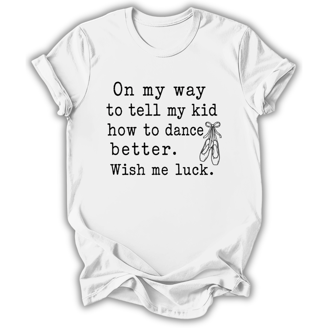 A white short-sleeve crewneck t-shirt with a black printed typewriter-style quote that reads 'On my way to tell my kid how to dance better. Wish me luck.