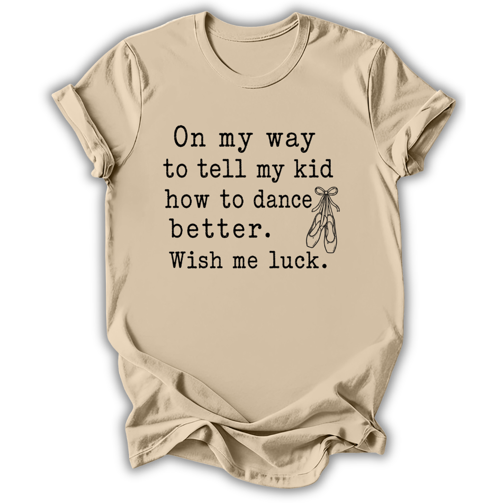 A beige short-sleeve t-shirt with a black printed typewriter-style quote that reads 'On my way to tell my kid how to dance better. Wish me luck.