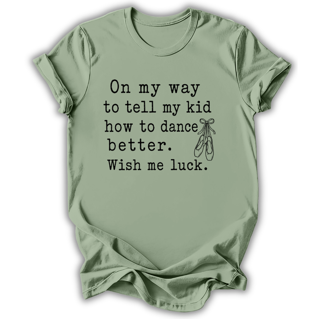 A sage green short-sleeve t-shirt with black printed text that reads 'On my way to tell my kid how to dance better. Wish me luck.