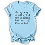 A light blue short-sleeve t-shirt with black printed text that reads 'On my way to tell my kid how to dance better. Wish me luck.