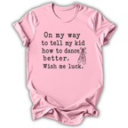 A light pink short-sleeve crewneck t-shirt with black printed text that reads 'On my way to tell my kid how to dance better. Wish me luck.