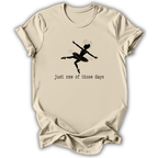 A beige short-sleeve t-shirt with a black graphic of a ballerina and the text 'just one of those days' printed on the front, displayed against a white background.