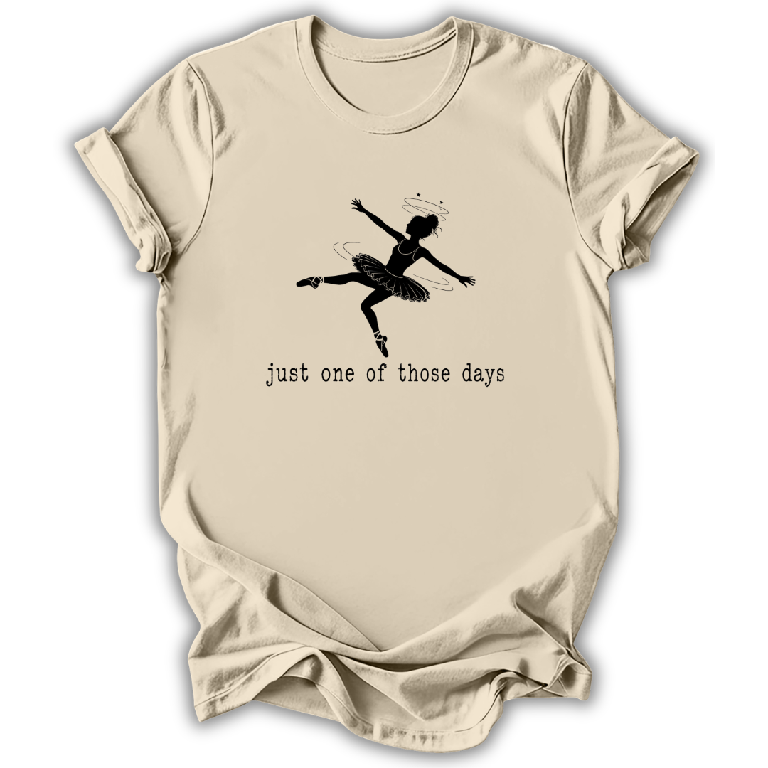 A beige short-sleeve t-shirt with a black graphic of a ballerina and the text 'just one of those days' printed on the front, displayed against a white background.