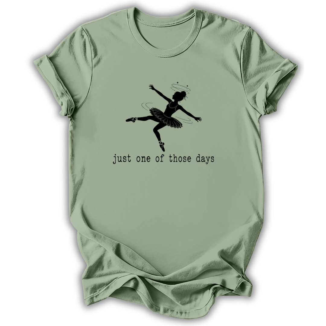 A sage green short-sleeve t-shirt with a black graphic of a ballerina and the text 'just one of those days' printed on the front, displayed against a clean white background.
