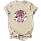 A beige short-sleeve t-shirt with a circular graphic on the chest that reads 'PROUD MEMBER OF The Bad Dance Moms CLUB'. The graphic features a pink striped circle with white text and small pink and white dance figures at the bottom.