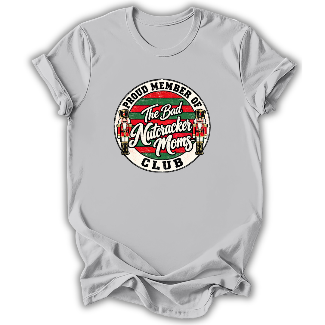 A light gray short-sleeve crewneck t-shirt featuring a circular graphic on the chest that reads 'PROUD MEMBER OF The Bad Nutcracker Moms CLUB' with nutcracker figures and red, green, and white details.