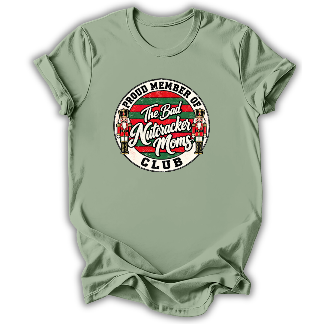 A sage green short-sleeve t-shirt with a circular graphic on the chest that reads 'Proud Member of The Bad Nutcracker Moms Club' featuring nutcracker illustrations.