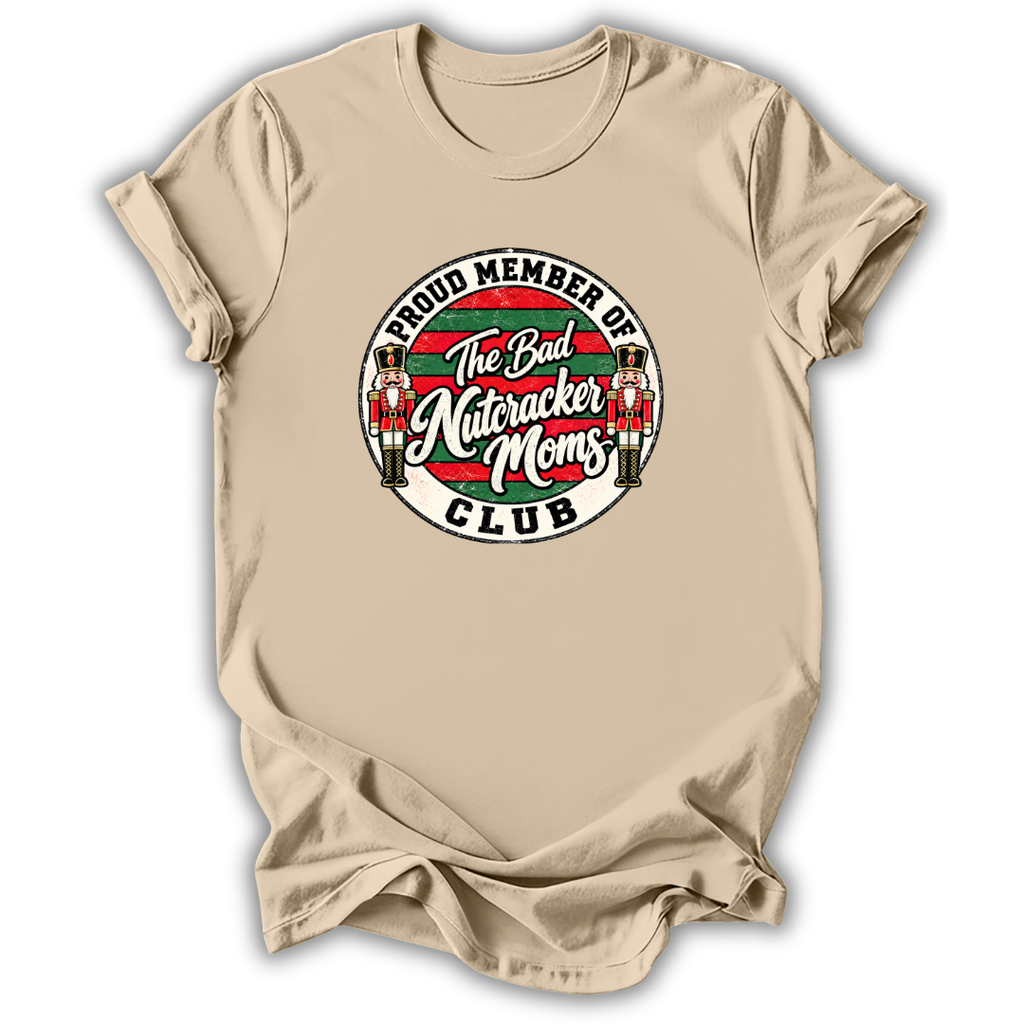 A beige short-sleeve t-shirt with a circular graphic on the chest that reads 'PROUD MEMBER OF The Bad Nutcracker Moms CLUB' with nutcracker figures and red, green, and white stripes.