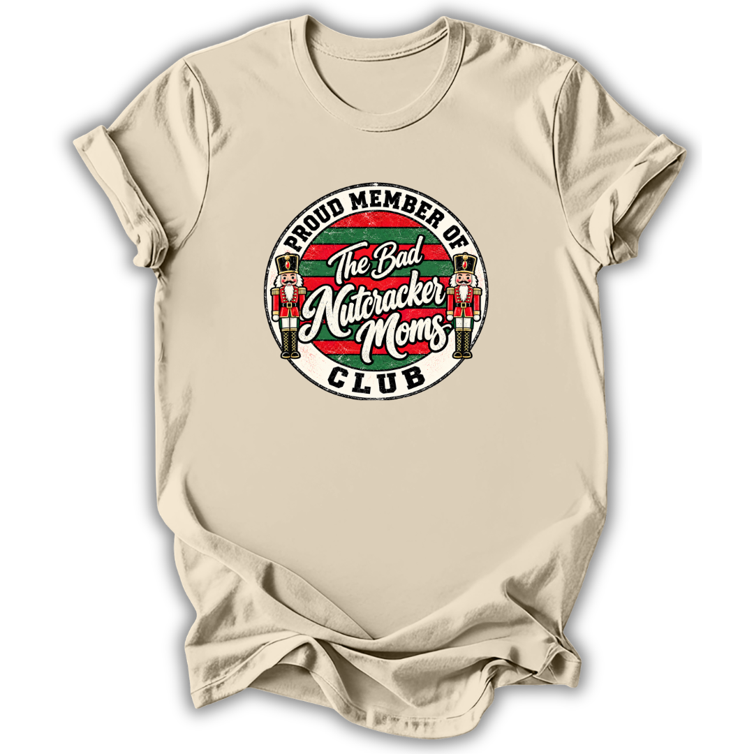 A beige short-sleeve t-shirt with a circular graphic on the chest that reads 'PROUD MEMBER OF The Bad Nutcracker Moms CLUB' with nutcracker illustrations.