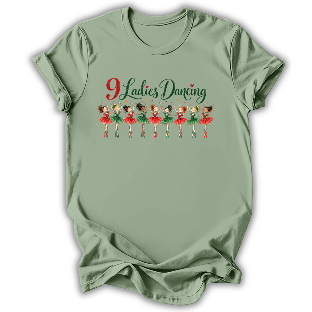 A sage green short-sleeve t-shirt with a graphic on the front that reads '9 Ladies Dancing' in red and green script above a row of cartoon ballerinas in red and green outfits, shown on a white background.
