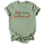 A sage green short-sleeve t-shirt with a graphic on the front that reads '9 Ladies Dancing' in red and green script above a row of cartoon ballerinas in red and green outfits, shown on a white background.