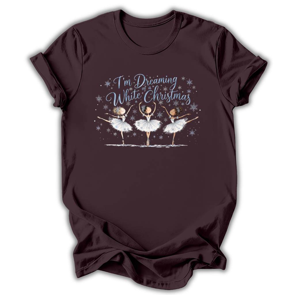 Brown short-sleeve t-shirt with a graphic print of three ballerinas and the text 'I'm Dreaming While Christmas' in blue and white, displayed on a clean white background.