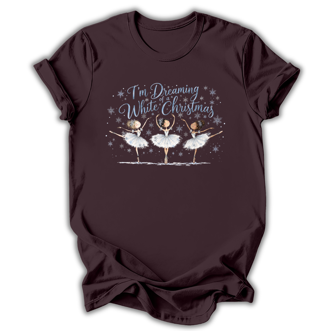Brown short-sleeve t-shirt with a graphic print of three ballerinas and the text 'I'm Dreaming While Christmas' in blue and white, displayed on a clean white background.