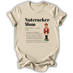 A beige graphic t-shirt laid flat on a white background, featuring a 'Nutcracker Mom' dictionary definition printed in black text next to an illustration of a nutcracker.