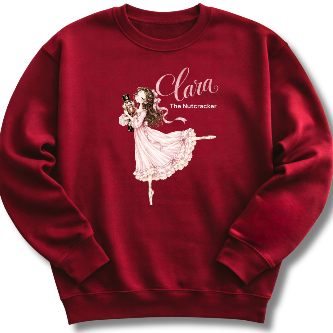 A maroon crewneck sweatshirt featuring an illustration of Clara in a graceful pink ballet pose with delicate 'The Nutcracker' lettering.
