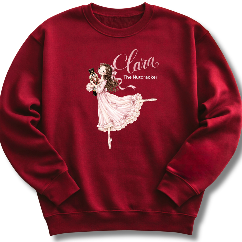 A maroon youth crewneck sweatshirt featuring an illustration of Clara in a graceful pink ballet pose with delicate 'The Nutcracker' lettering.