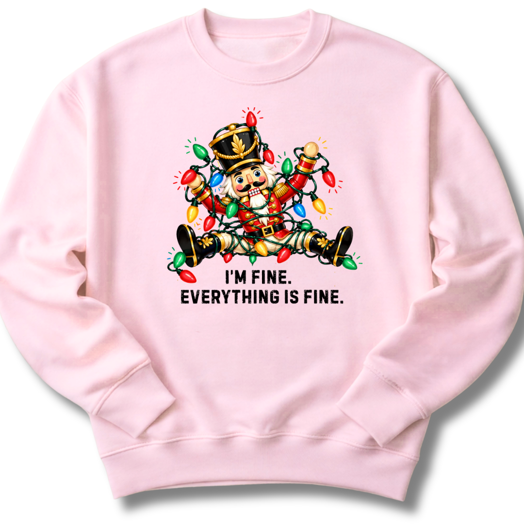 A light pink crewneck sweatshirt featuring a colorful nutcracker tangled in Christmas lights beneath the words 'I'm fine. Everything's fine.'