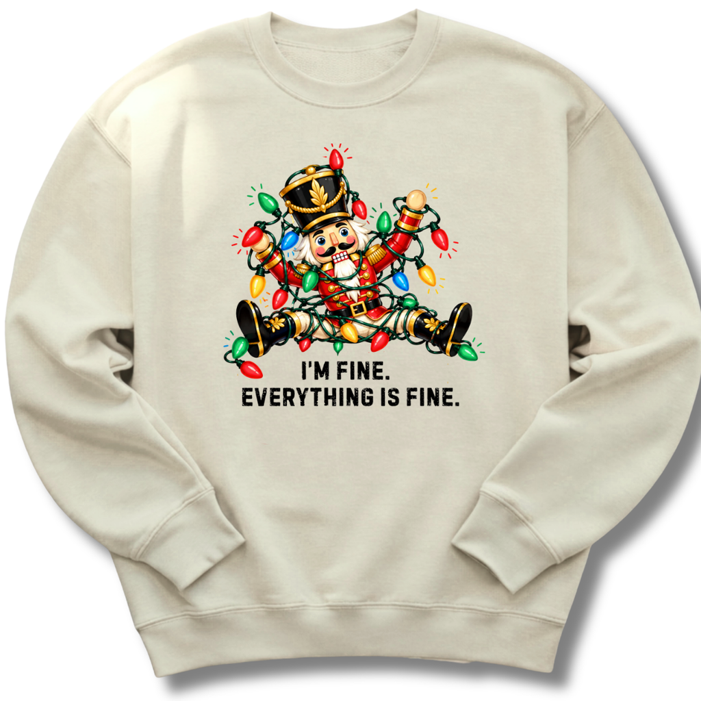 A sand-colored crewneck sweatshirt featuring a colorful nutcracker tangled in Christmas lights beneath the words 'I'm fine. Everything's fine.'