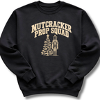 A black crewneck sweatshirt featuring a vintage-inspired 'Nutcracker Prop Squad' design with a nutcracker soldier and a Christmas tree.