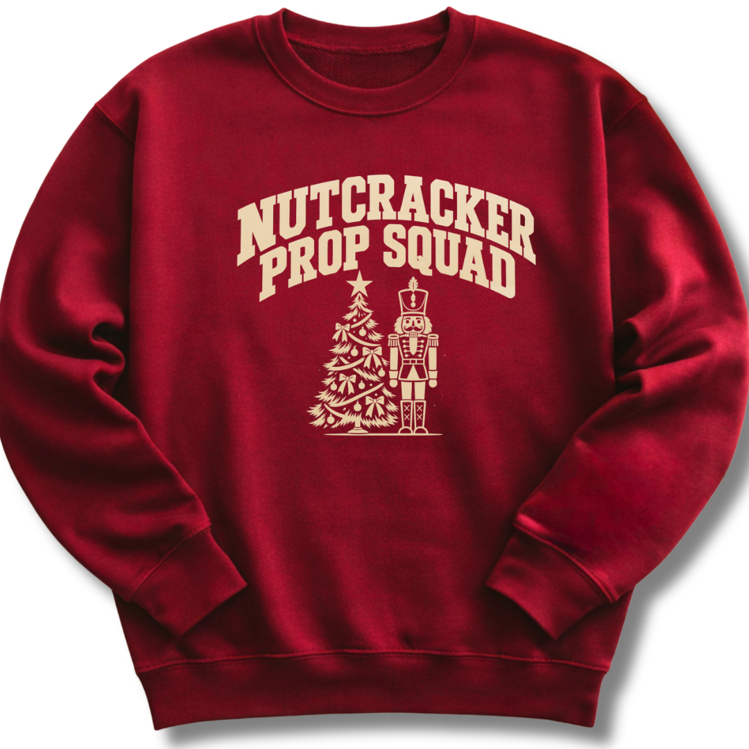 A maroon crewneck sweatshirt featuring a vintage-inspired 'Nutcracker Prop Squad' design with a nutcracker soldier and a Christmas tree.