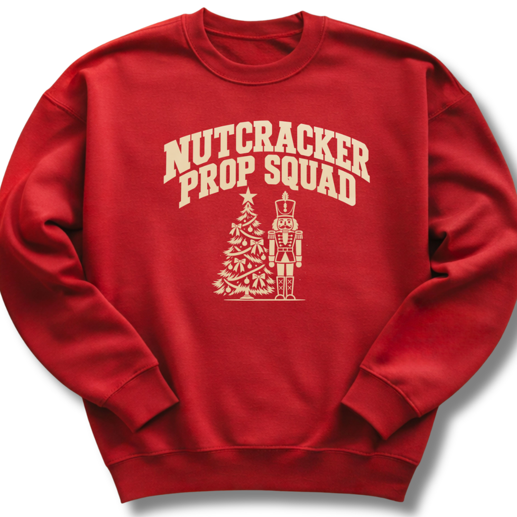 A red crewneck sweatshirt featuring a vintage-inspired 'Nutcracker Prop Squad' design with a nutcracker soldier and a Christmas tree.
