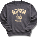 A dark heather gray crewneck sweatshirt featuring a vintage-inspired 'Nutcracker Prop Squad' design with a nutcracker soldier and a Christmas tree.
