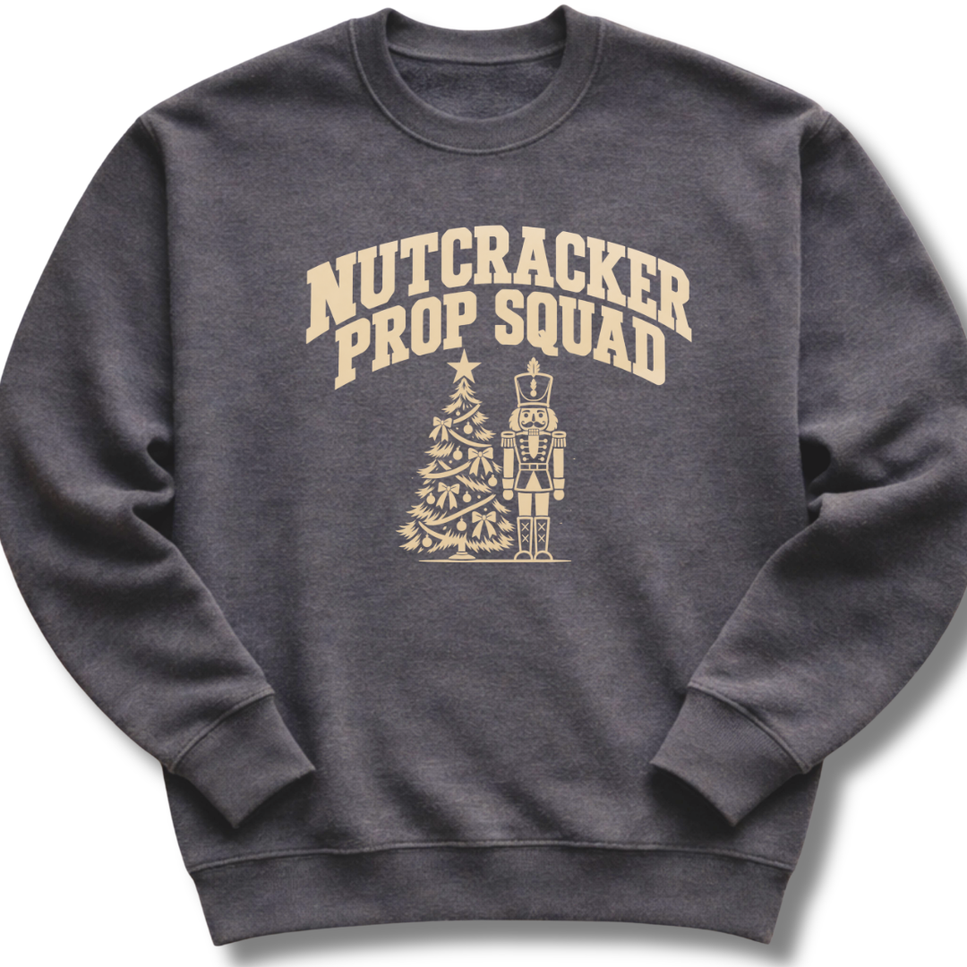 A dark heather gray crewneck sweatshirt featuring a vintage-inspired 'Nutcracker Prop Squad' design with a nutcracker soldier and a Christmas tree.