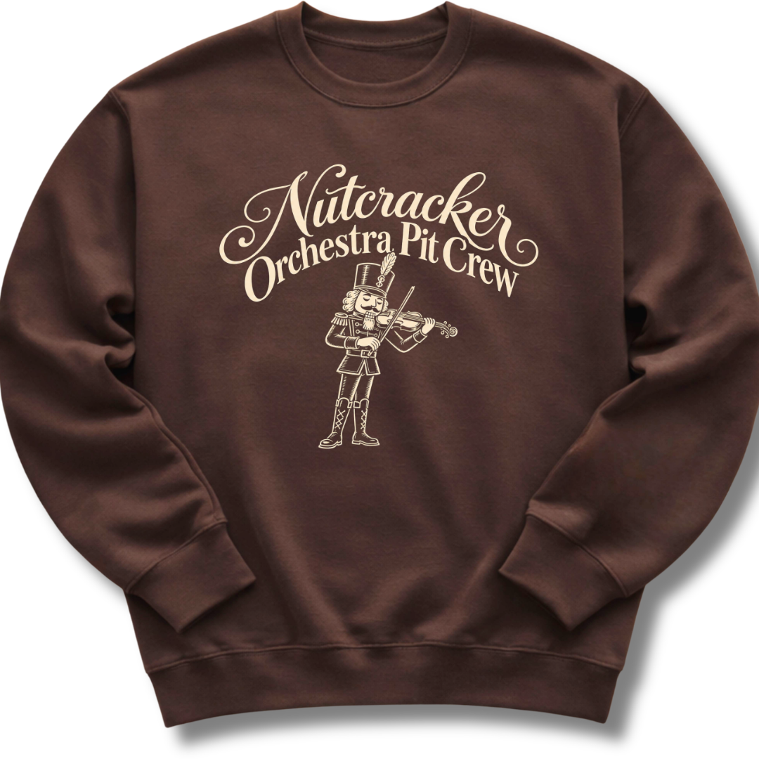 A dark brown crewneck sweatshirt featuring a 'Nutcracker Orchestra Pit Crew' design with a classic nutcracker and elegant script lettering.