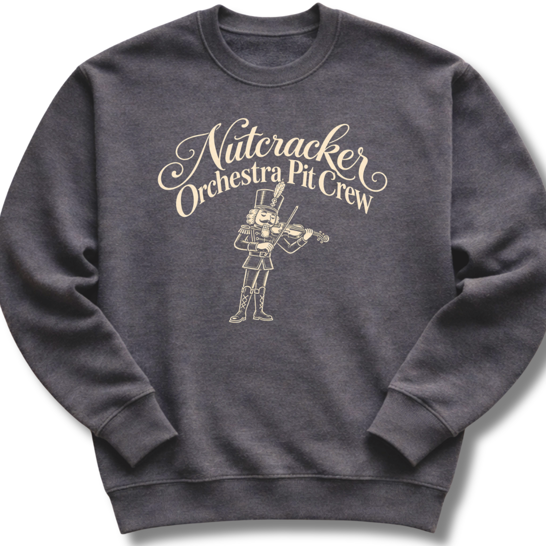 A dark heather gray crewneck sweatshirt featuring a 'Nutcracker Orchestra Pit Crew' design with a classic nutcracker and elegant script lettering.