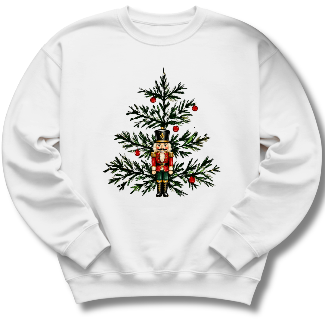 A white crewneck sweatshirt featuring a nutcracker nestled among evergreen branches and bright red winter berries.