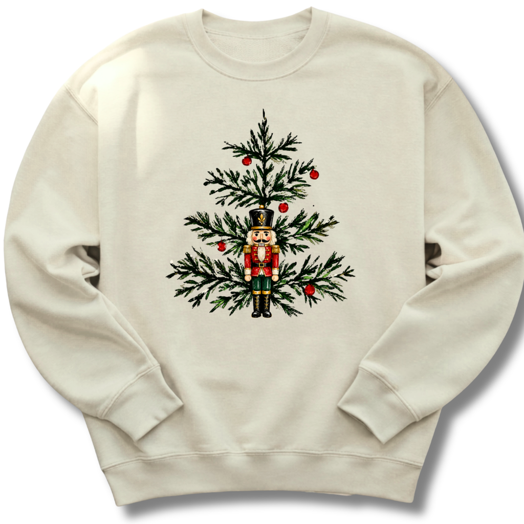 A sand-colored crewneck sweatshirt featuring a nutcracker nestled among evergreen branches and bright red winter berries.