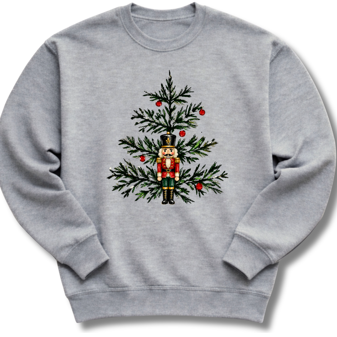 A heather gray crewneck sweatshirt featuring a nutcracker nestled among evergreen branches and bright red winter berries.