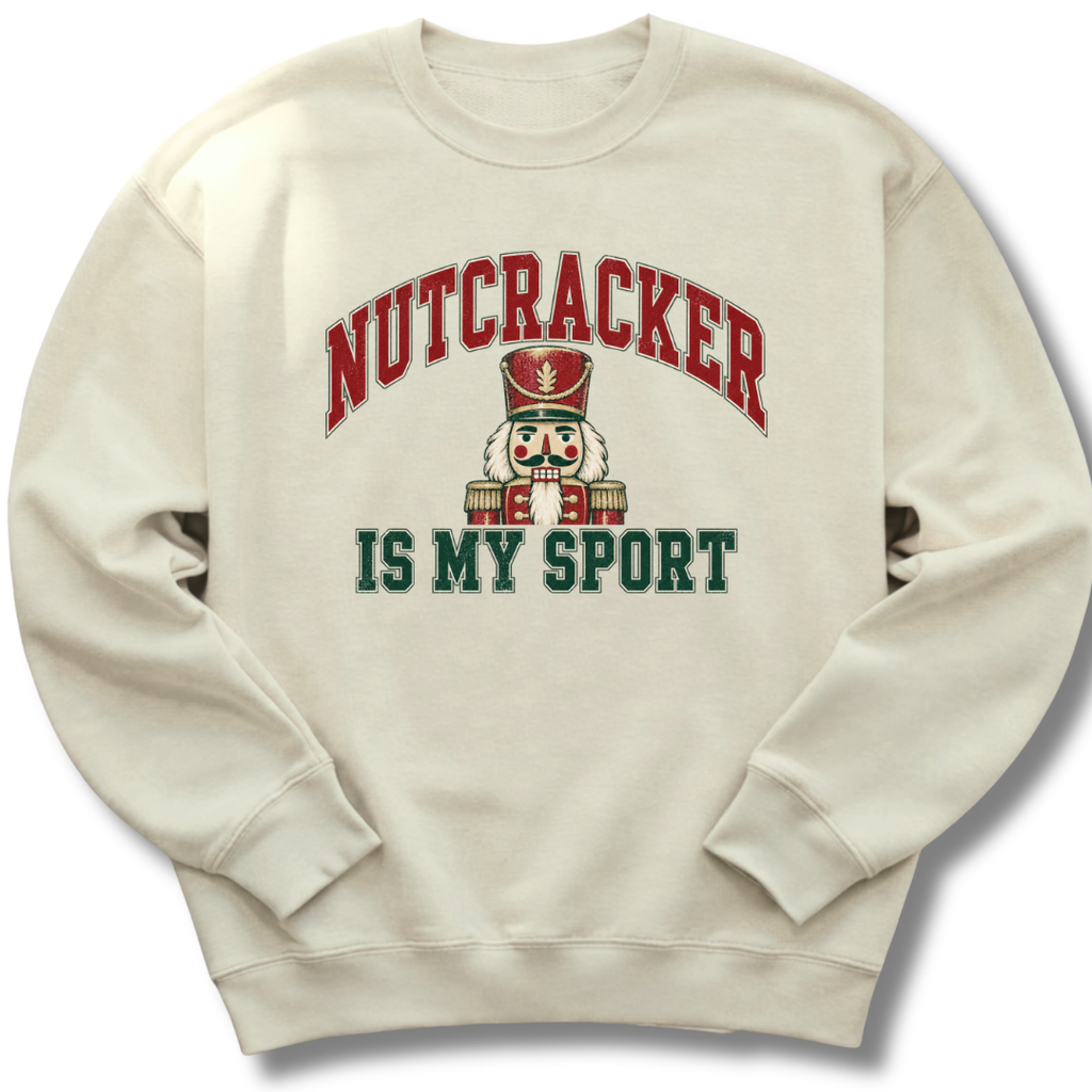 A sand-colored crewneck sweatshirt featuring a playful nutcracker graphic with the words 'Nutcracker Is My Sport'.