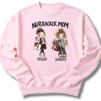 A light pink crewneck sweatshirt featuring an illustrated 'Nutcracker Mom' design with two characters, one ready for Friday's performance and one twirling into Sunday.