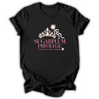 A black short-sleeve t-shirt with a graphic print on the front featuring a gold crown, a white ribbon, and the text 'SUGARPLUM PRIVILEGE' and 'SOME OF US ARE FLOWERS' in pink and white.