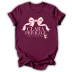 A maroon short-sleeve t-shirt with a pink graphic on the front featuring a bow, the text 'CLARA PRIVILEGE.', and 'SOME OF US ARE MICE.