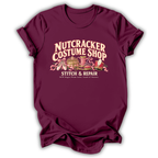 A maroon short-sleeve t-shirt printed with the “Nutcracker Costume Shop” graphic design.