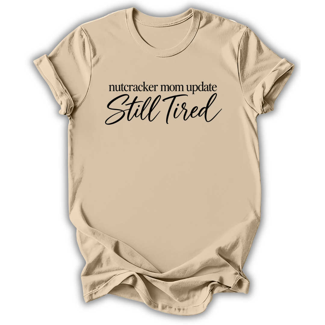 A sand beige short-sleeve t-shirt printed with the “Still Tired Nutcracker Mom” graphic design.