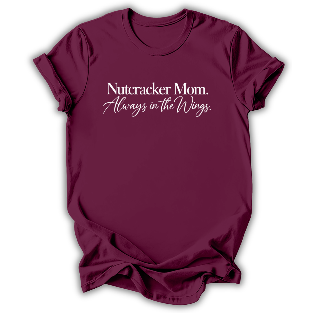 A maroon short-sleeve t-shirt printed with the “Nutcracker Mom Always in the Wings” graphic design.