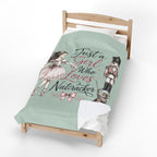 A mint green bedding set on a wooden toddler bed, featuring a printed design with a ballerina, a nutcracker, and the text 'Just a Girl Who Loves Nutcracker' in black and pink script.
